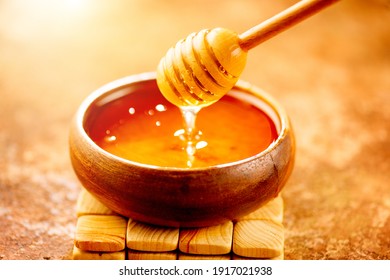 Honey dripping from honey dipper in wooden bowl.  Close-up. Healthy organic Thick honey dipping from the wooden honey spoon, closeup.