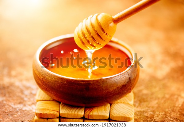 Honey dripping from honey dipper in wooden bowl.\
 Close-up. Healthy organic Thick honey dipping from the wooden\
honey spoon, closeup.