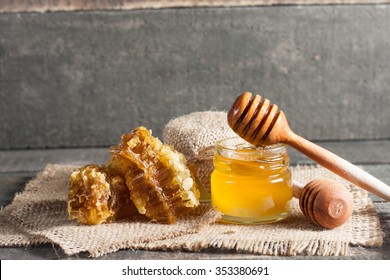 Honey dripping from a wooden honey dipper in a jar on wooden grey rustic background