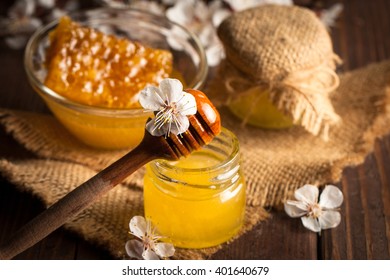Honey dripping from a wooden honey dipper in a jar on wooden grey rustic background. Propolis and bee honey. Spring natural product concept.