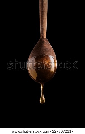 Honey dripping from a wooden spoon on black background.
