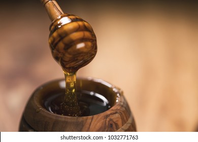 honey drips from dipper into wooden pot