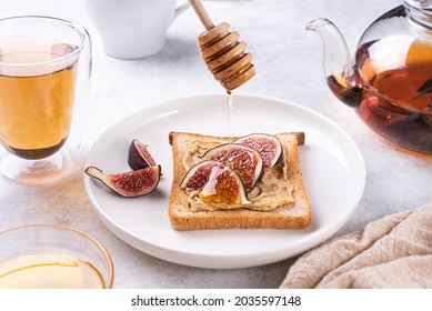 Honey Flowing Down To Toast With Peanut Butter And Slices Of Figs On A Plate On A White Plate, Healthy Breakfast, Close-up.