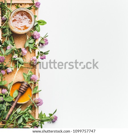 Honig im Glas mit Schöpflöffel, Bienenwaben und wilden Blumen