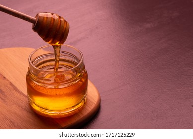 Honey in jar with wooden honey dipper on the table.