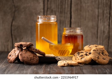 Honey in open jars and in a bowl, dipper and homemade cookies with chocolate chips on a wooden background. Homemade cakes and honey for breakfast. Composition of craft chocolate cookies and honey. - Powered by Shutterstock