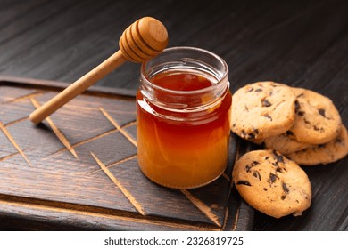 Honey in open jars and in a bowl, dipper and homemade cookies with chocolate chips on a wooden background. Homemade cakes and honey for breakfast. Composition of craft chocolate cookies and honey. - Powered by Shutterstock