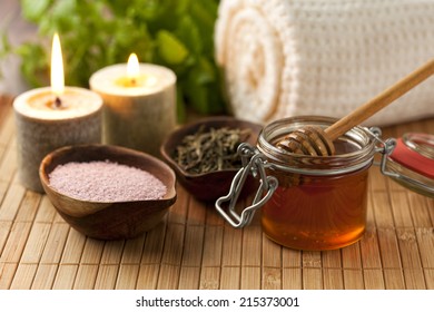 Honey and other bath ingredients with candles and rolled towel