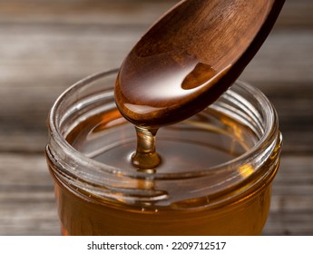 Honey and wooden spoon in glass container on old wooden background. Honey dripping from spoon. 