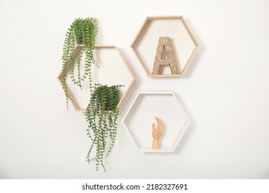 Honeycomb shaped shelves with decorative elements and houseplants on white wall