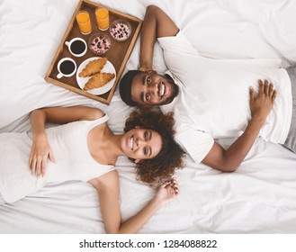 Honeymoon concept. Happy black young couple lying in bed in morning with breakfast, top view - Powered by Shutterstock