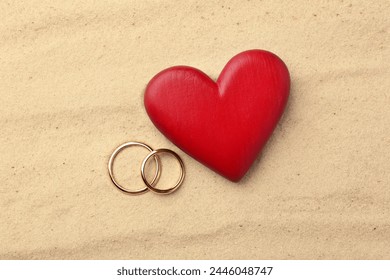 Honeymoon concept. Two golden rings and red wooden heart on sand, top view - Powered by Shutterstock