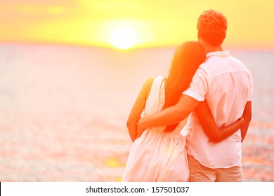 Honeymoon couple romantic in love at beach sunset. Newlywed happy young couple embracing enjoying ocean sunset during travel holidays vacation getaway. Interracial couple, Asian woman, Caucasian man. - Powered by Shutterstock