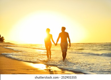 Honeymoon romantic couple in love holding hands walking on beautiful sunset at beach in waterfront. Lovers or newlywed married young couple by the sea enjoying relaxed vacation travel holiday. Hawaii. - Powered by Shutterstock