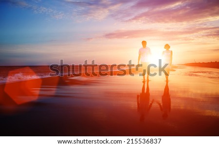 Honeymoon romantic couple in love walking on the beach on orange sunset background, happy young couple embracing enjoying ocean sunset during travel holidays vacation