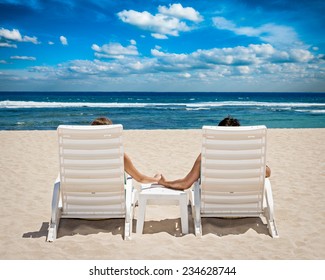 Honeymoon travel resort concept - couple in beach chairs holding hands near ocean