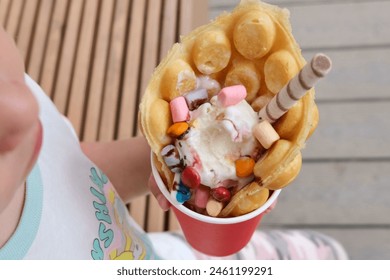 Hong Kong or bubble waffles with ice cream, chocolate tubes and marmalade in the hands of a child - Powered by Shutterstock