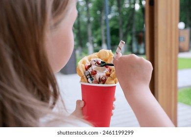 Hong Kong or bubble waffles with ice cream, chocolate tubes and marmalade in the hands of a child - Powered by Shutterstock