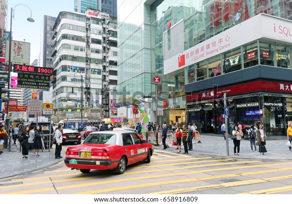 HONG KONG, CHINA - APRIL 27; Busy street in\
Hong Kong with traffic and pedestrians crossing road in Hong Kong,\
China - April 27, 2017: Traditional red taxi and other cars on one\
of busy city junctions