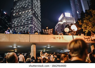 Hong Kong, China - Oct 26, 2019: Masked, anti government protester holding a black flag with "Free Hong Kong, Revolution of our Time," on it at Chater Garden at night. 