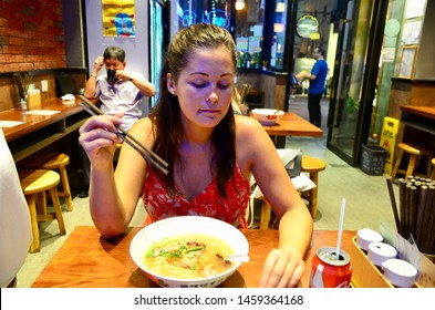Hong Kong, China - September 14, 2018. Dark haired mixed raced woman in her 20s wearing summer red dress eating a bowl of noodles in a Hong Kong restaurant in September 2018.