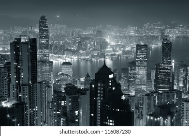 Hong Kong city skyline at night with Victoria Harbor and skyscrapers illuminated by lights over water viewed from mountain top in black and white. - Powered by Shutterstock