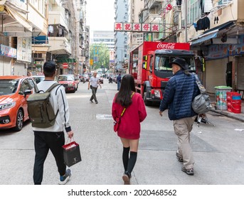 HONG KONG, HONG KONG - Jul 24, 2018: Three Unrelated People Walking Away From Camera On A Hong Kong Street   She Is Wearing Bright Red Short Dress   Looking Down A Long Street With Traffi