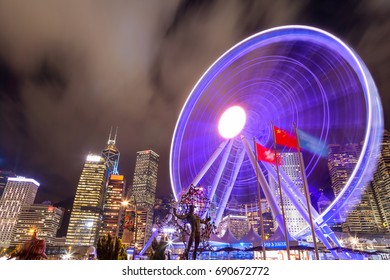 HONG KONG, JULY 10, 2017: Long Exposure Of The Spinning Observation Wheel At Hong Kong's Central Pier Near Victoria Harbour With The Downtown Financial District In The Background.
