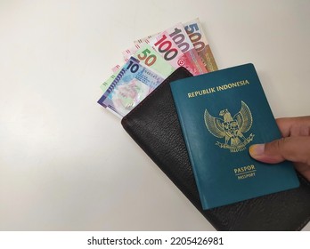 Hong Kong, September 2022 : 10.50.100.500 Hong Kong Dollar Currency Flanked By Brown Wallet And Green Indonesian Passport Book In Human Hand Isolated On White Background.