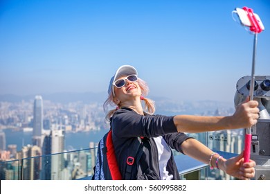 Hong Kong Victoria Peak Tourist Taking Selfie Stick Picture Photo With Smartphone Enjoying View Over Victoria Harbour. Young Happy Woman Travel In Asia.Viewing Platform On Top Of Peak Tower, Hong Kong