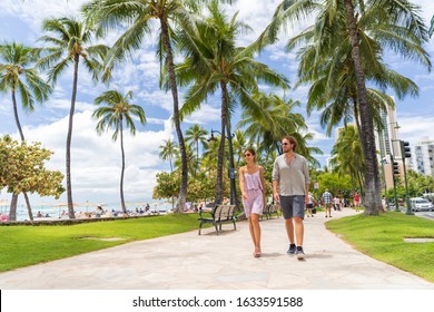 Honolulu city travel tourists couple walking on Waikiki beach boardwalk visiting Oahu island, USA summer travel holidays. Happy man and woman lifestyle.