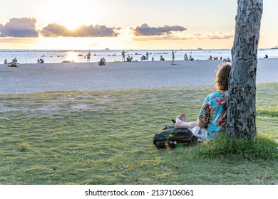 Honolulu, Hawaii - circa February 2022: A man sits against a tree and enjoys watching the sunset at at Ala Moana Beach Park.