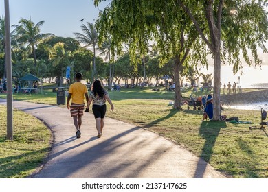 Honolulu, Hawaii - circa February 2022: People enjoy a relaxing day at Ala Moana Beach Park. They walk along a path at sunset.