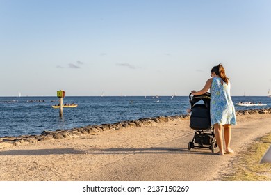 Honolulu, Hawaii - circa February 2022: A woman pushes a stroller along the ocean at Ala Moana Beach Park.