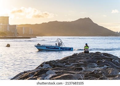 Honolulu, Hawaii - circa February 2022: A woman watches boats pass at sunset, relaxing at Ala Moana Beach Park.
