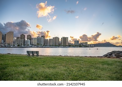 Honolulu, Hawaii - circa February 2022: A bench in focus overlooking 
the beautiful city skyline from Ala Moana harbor.