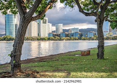 Honolulu, Hawaii - circa February 2022: A bench in focus at Ala Moana park, with the beautiful city skyline in the distance.