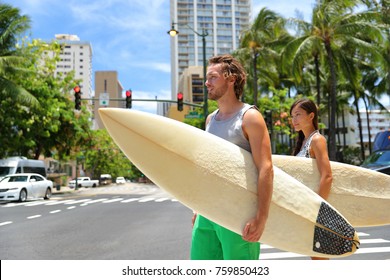 Honolulu Hawaii Lifestyle Surfers People Walking In City With Surfboards Going To The Beach Surfing. Outside Hawaiian Surf Living. Surfer Couple Crossing Street. Waikiki, Honolulu, Oahu, Hawaii, USA.