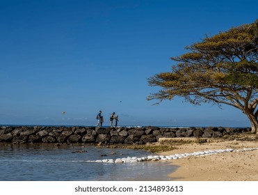 Honolulu, Hawaii, USA.  March 12, 2022.  Waikiki Vacation With A Family Walking On A Lava Break Wall With Parasails In The Background.