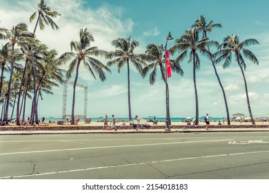 HONOLULU, UNITED STATES - APRIL 2022 : People Walking On Waikiki Beach With Palm Trees And City Street In Honolulu, Hawaii