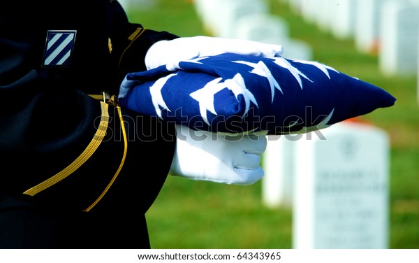 Honor Guard holding folded American\
flag at grave site at Arlington National\
Cemetery