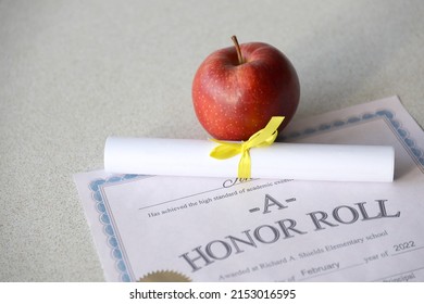 A honor roll lies on table with small scroll and red apple. Education documents close up