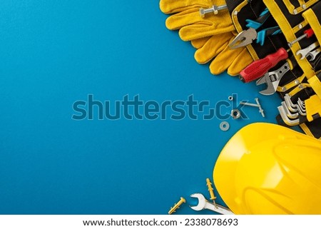 Honoring contributions of construction workers on Labor Day: this top-view photo featuring flag, construction helmet, work gloves and building tool on blue backdrop. Ideal for advertisements or text