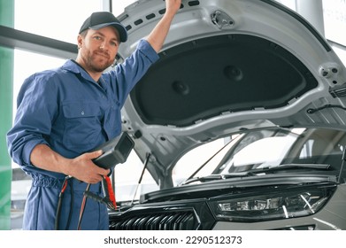 With hood opened. Man in blue uniform is working in the car service. - Powered by Shutterstock