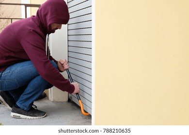 Hooded Burglar Forcing Window Shutter Lock