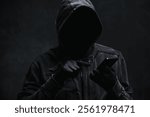 Hooded computer hacker using smartphone, selective focus