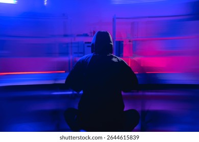 A hooded figure is focused on coding in a dark environment, surrounded by dynamic lights. This image symbolizes the pressing issues of security and cyber threats in cloud networks.