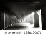 A hooded figure looking down on a path on a foggy winters night. With a grainy vintage, muted edit.