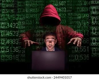 A hooded figure sits behind a laptop, surrounded by a matrix of green binary code. - Powered by Shutterstock