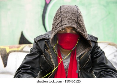 Hooded figure, wearing a scarf in front of his nose and mouth to disguise himself, looking menacing into the camera